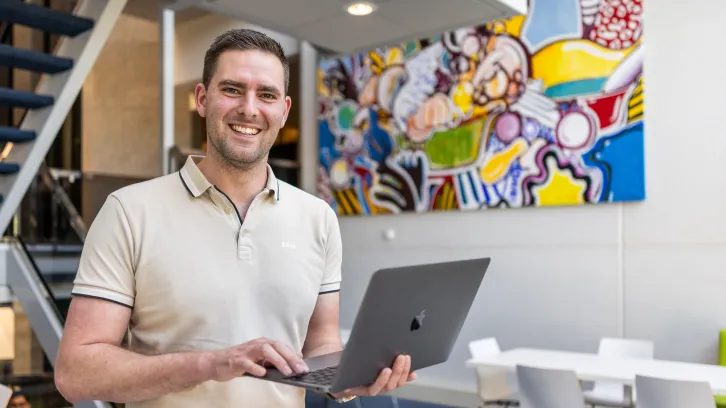 Edwin Brongers met laptop in de hand voor een kleurig schilderij